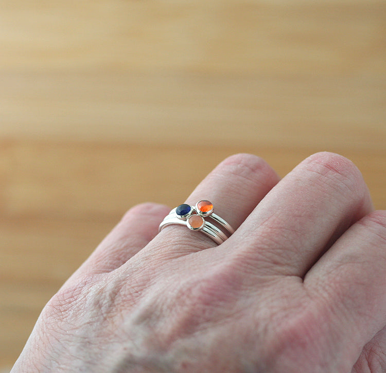 Ethical blue sapphire and orange stacking rings in sterling silver on finger. Handmade in the US.